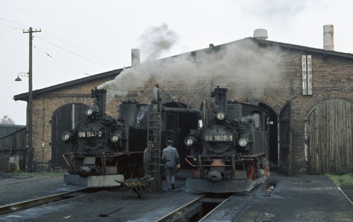 99 1542 neben 99 1608 in einer Ruhepause und beim Restaurieren an vielfotografierter Stelle vor den Schuppentoren in Mügeln, am Nachmittag des 26.10.1977
