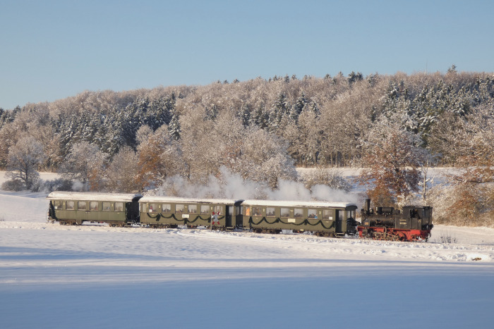 99 7203 Tv mit Nikolauszug auf Talfahrt zurück von Oppingen nach Amstetten an einem schneebedeckten Feldweg-Bahnübergang am oberen Duital, um 15:14h am 03.12.2023