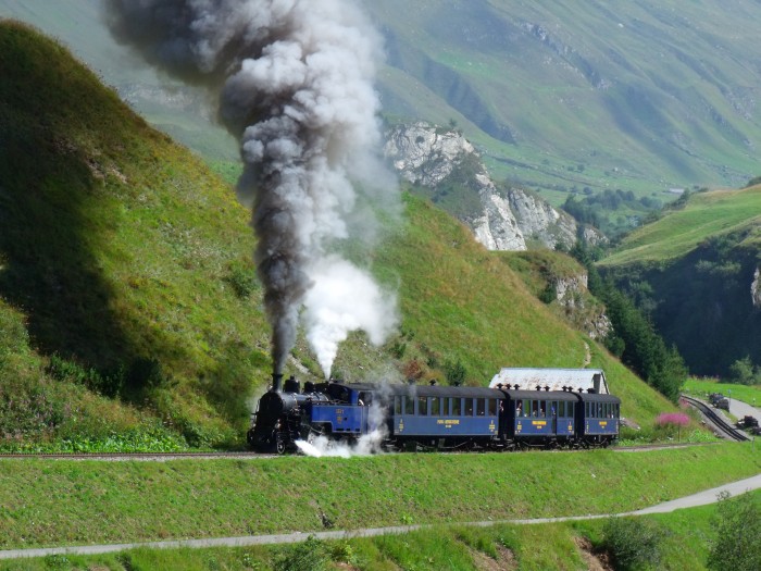 DFB 1 mit erstem Zug des Tages von Realp nach Oberwald, fotografiert und akustisch aufgenommen am Beginn des Zahnstangenabschnitts (weit hinten auf dem Foto sichtbar!), kurz vor den Brücken über die Furkareuss (Straße und Bahn direkt nebeneinander), um 10:29h am 22.08.2014
