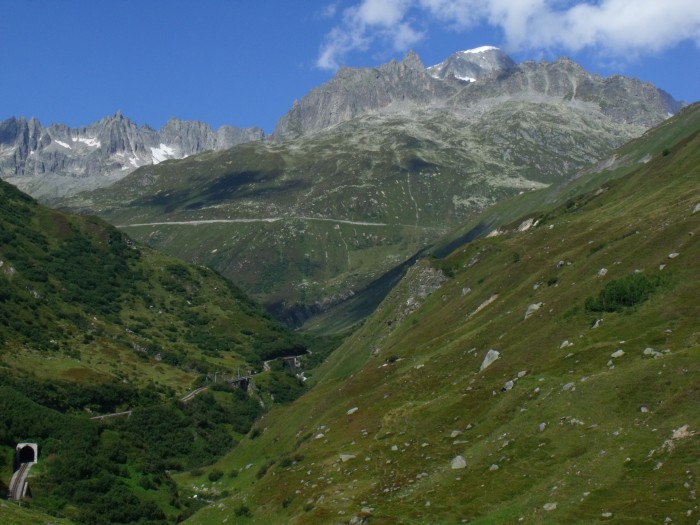 Links am Talrand der Alt Senntumstafeltunnel I (der oberste von den drei Tunneln), dahinter die Klappbrücke vom Steffenbachtal und ganz hinten am Berghang die Stützmauer der Paßstraße vor der Kulisse der Berggipfel am Furkapass