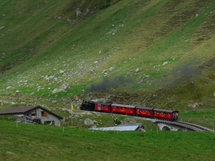 B.F.D. 9 mit Zug Nr.133 nach Oberwald, direkt hinter dem Steinstafelviadukt, links der kleine Alm-Hof, von wo in den Sommermonaten die im Tal überall grasenden Rinder überwacht bzw. gehütet werden. Im Winter ist das alles hier unter meterhohem Schnee begraben und daher natürlich kein Betrieb, auch nicht auf dem kleinen Bauernhof, um 10:47h am 25.08.2017