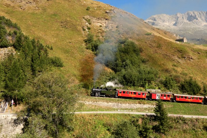704  mit Zug Nr.133 Realp->Oberwald auf dem Bahndamm am Nordhang vor den Wilerbrücken, um 10:27h am 13.08.2022