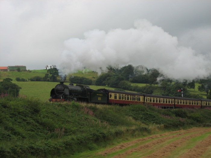 825 mit Zug aus Whitby nach Pickering nimmt Anlauf in die Steigung hinter den “sheds” hinter Grosmont, fotografiert von der Wiese gegenüber den Esk Valley Cottages, um 14:39h am 18.08.2008